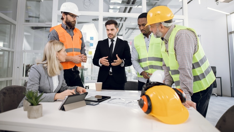 A group of construction professionals in safety gear collaborating with a business manager around a table, discussing project plans