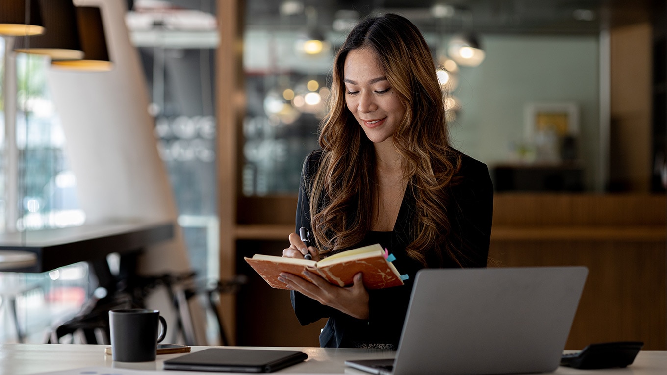 A person sitting at a desk with a laptop computer, reading about new features in QuickBooks Online.